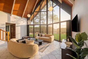 A living room with a couch looking out pitched double-height ceiling lined with timber to the grassed front yard.