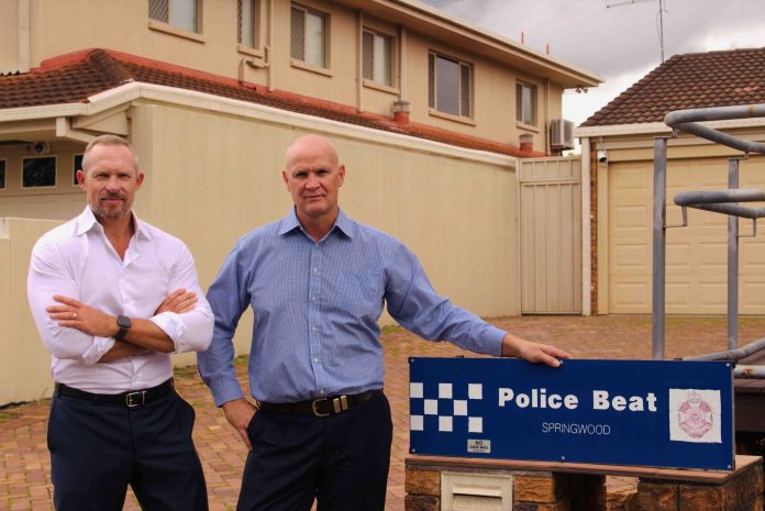 Two men in business clothes stand out the front of a houise next door to a unit block.